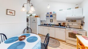 Cozinha compacta com armários brancos, uma mesa de jantar com toalha azul e luminária pendente.