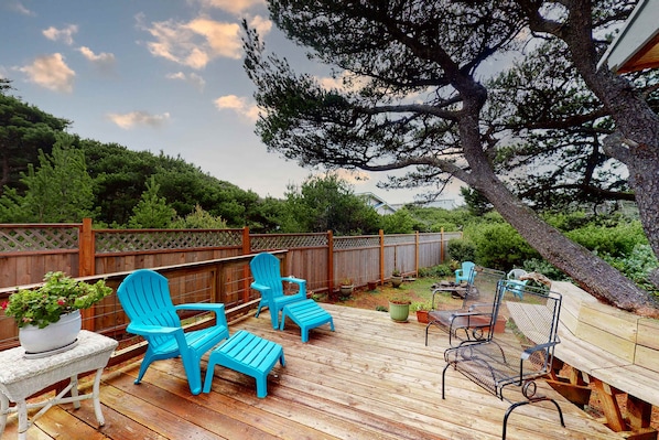 A wooden deck with blue Adirondack chairs, a wicker table, and a metal bench.