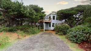 Uma casa com entrada de automóveis em cascalho, cercada por vegetação densa e árvores.