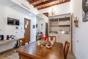 A dining area with a wooden table, chairs, a TV, and a kitchen in the background. - iFlat | Antonella House Trevi Terrace Hideaway (Rome)