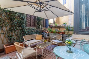 A patio with wicker furniture, a table with a vase of flowers, and a large umbrella. - iFlat | Antonella House Trevi Terrace Hideaway (Rome)