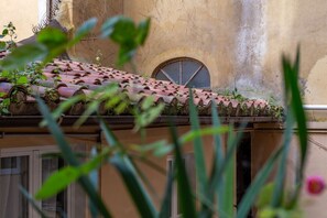 A building with a tiled roof, a window with a metal shutter, and some greenery in the foreground. - iFlat | Antonella House Trevi Terrace Hideaway (Rome)