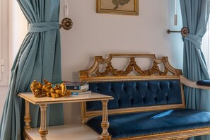 A room with a blue upholstered sofa, a table with books and a golden statue, and curtains tied back. - iFlat | Antonella House Trevi Terrace Hideaway (Rome)