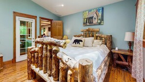 Un dormitorio con estructura de cama de madera, una puerta con paneles de vidrio, un cuadro en la pared y una mesita de noche con lámpara.
