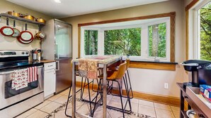 Una cocina con comedor, refrigerador y ventana con vista a árboles.