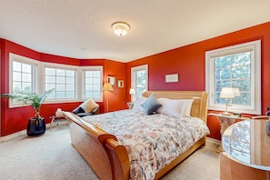 A bedroom with a large bed, two bedside tables, a nightstand, a potted plant, and a window with a view.