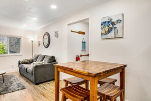 A dining area with a wooden table and benches, a gray sofa, a clock, and a framed artwork on the wall. - Single-level home with firepit & gas fireplace - walk to the beach, 3 dogs OK (Ocean Park)