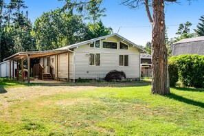 A single-story house with a porch, a small front yard, and a tree. - Single-level home with firepit & gas fireplace - walk to the beach, 3 dogs OK (Ocean Park)