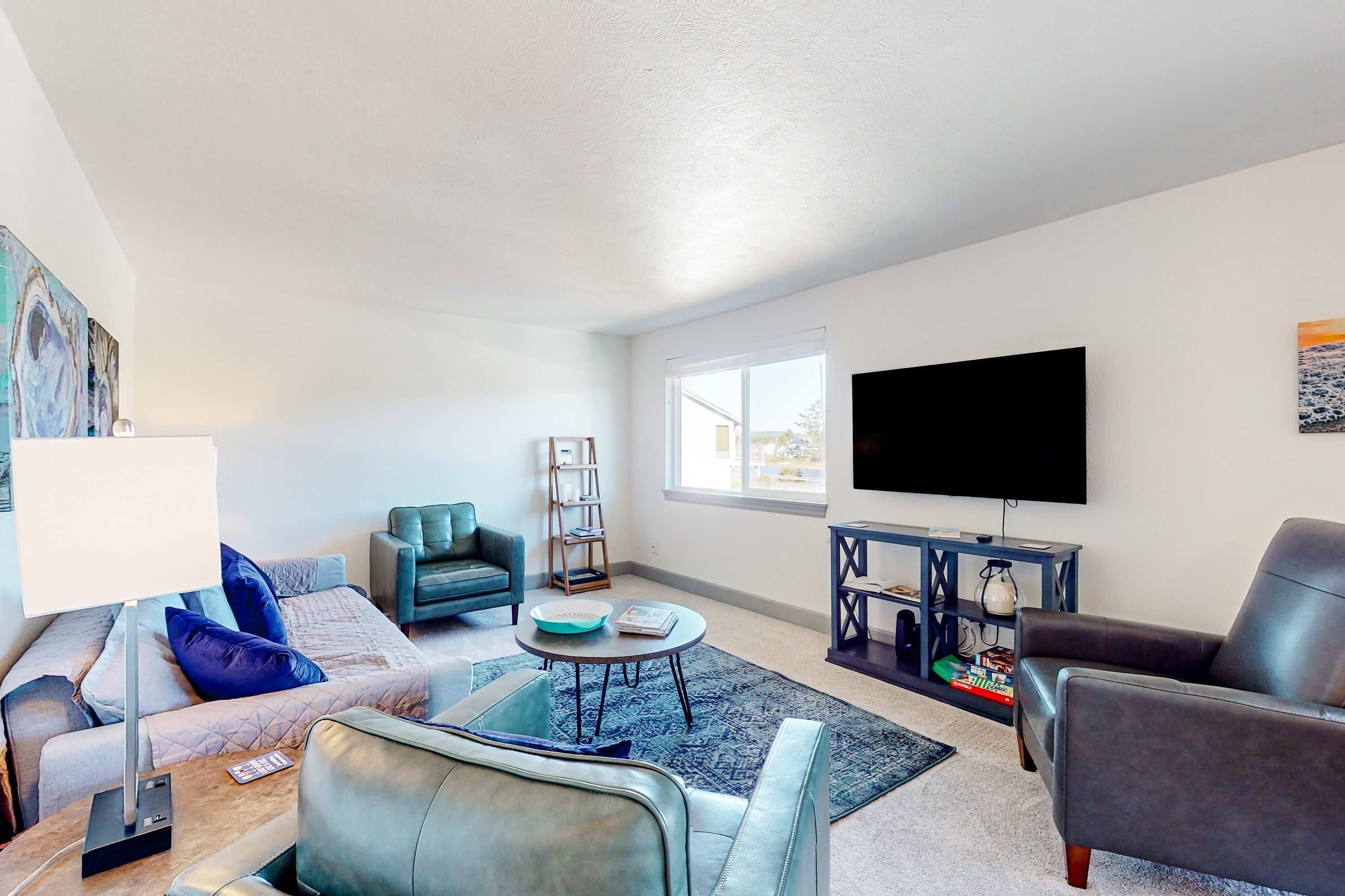 A living room with a sofa, armchair, coffee table, TV, bookshelf, and a window.