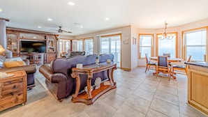 A spacious living room with a large television, leather sofa, wooden console table, and a dining area with a view of the ocean. - Gorgeous oceanfront estate with amazing views & hot tub - steps to quiet beach (Brookings)