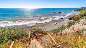 A coastal view with a wooden staircase leading to a beach, clear skies, and calm sea. - Gorgeous oceanfront estate with amazing views & hot tub - steps to quiet beach (Brookings)