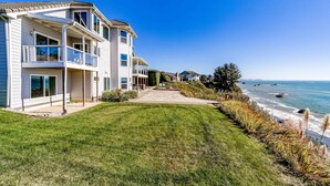 A coastal residential building with a balcony, a paved pathway, and a view of the ocean. - Gorgeous oceanfront estate with amazing views & hot tub - steps to quiet beach (Brookings)