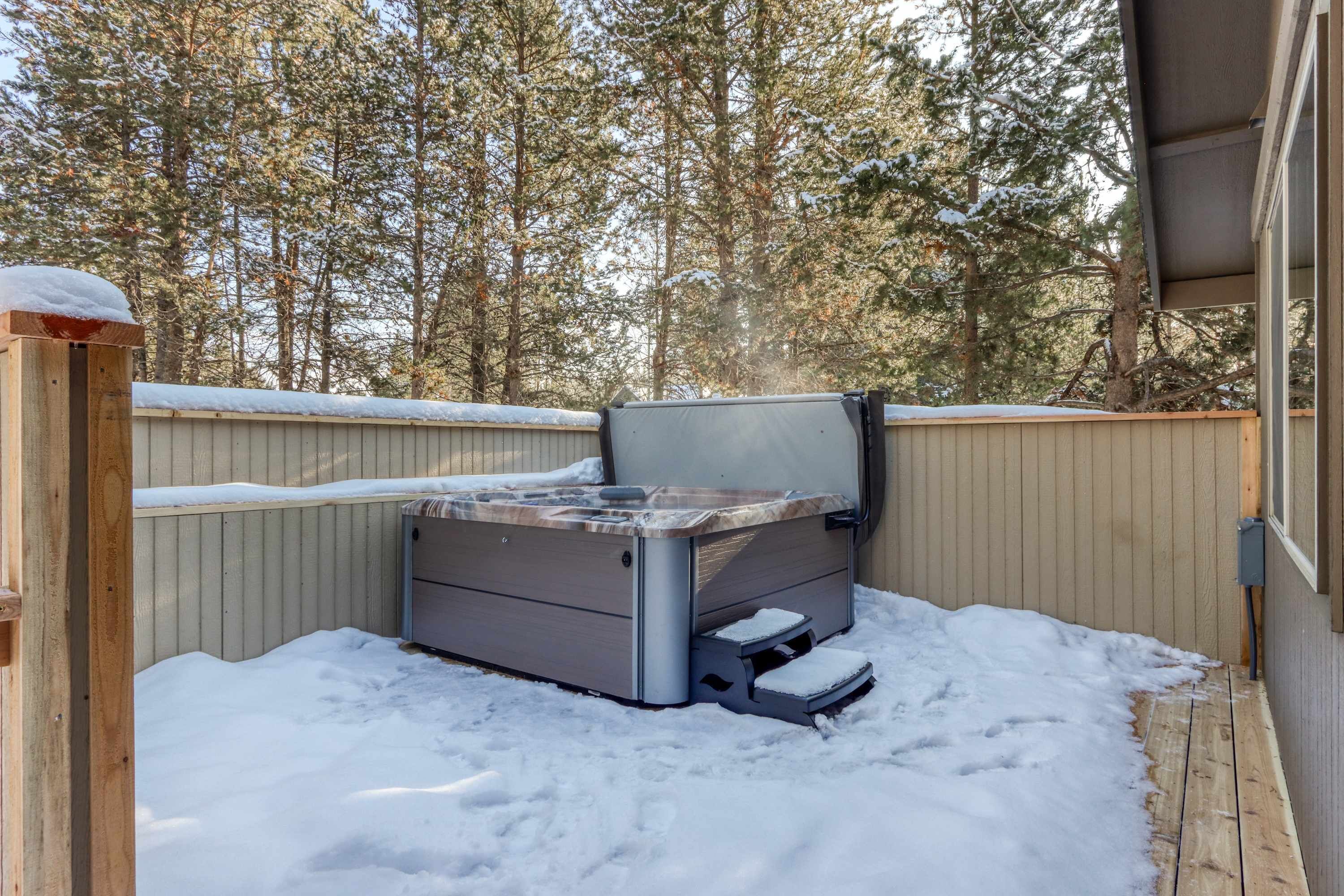 A hot tub in a snowy outdoor area with a wooden deck and a wooden fence.