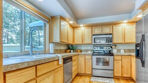 A modern kitchen with wooden cabinets, stainless steel appliances, and a large window. - Lovely home near town with private hot tub, scenic deck, W&D, & chic decor (Sunriver)