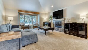A living room with a sectional sofa, a coffee table, a fireplace, and a TV mounted on the wall. - Lovely home near town with private hot tub, scenic deck, W&D, & chic decor (Sunriver)