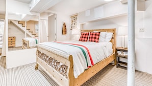 Un dormitorio con cama de madera, mesita de noche, estante en la pared, escalera y luz de techo.