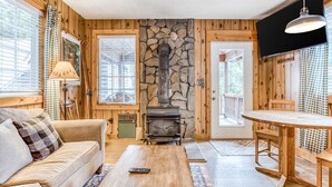 Una habitación acogedora con chimenea de piedra, paredes de madera, un sofá, una mesa de comedor y un televisor.