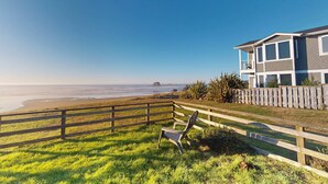A beach view with a wooden fence, a chair, and a house with a balcony.