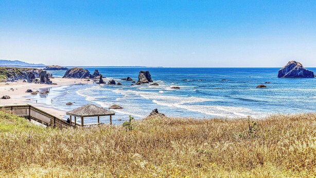 A coastal beach with rocky outcrops, a wooden pier, and a gazebo.