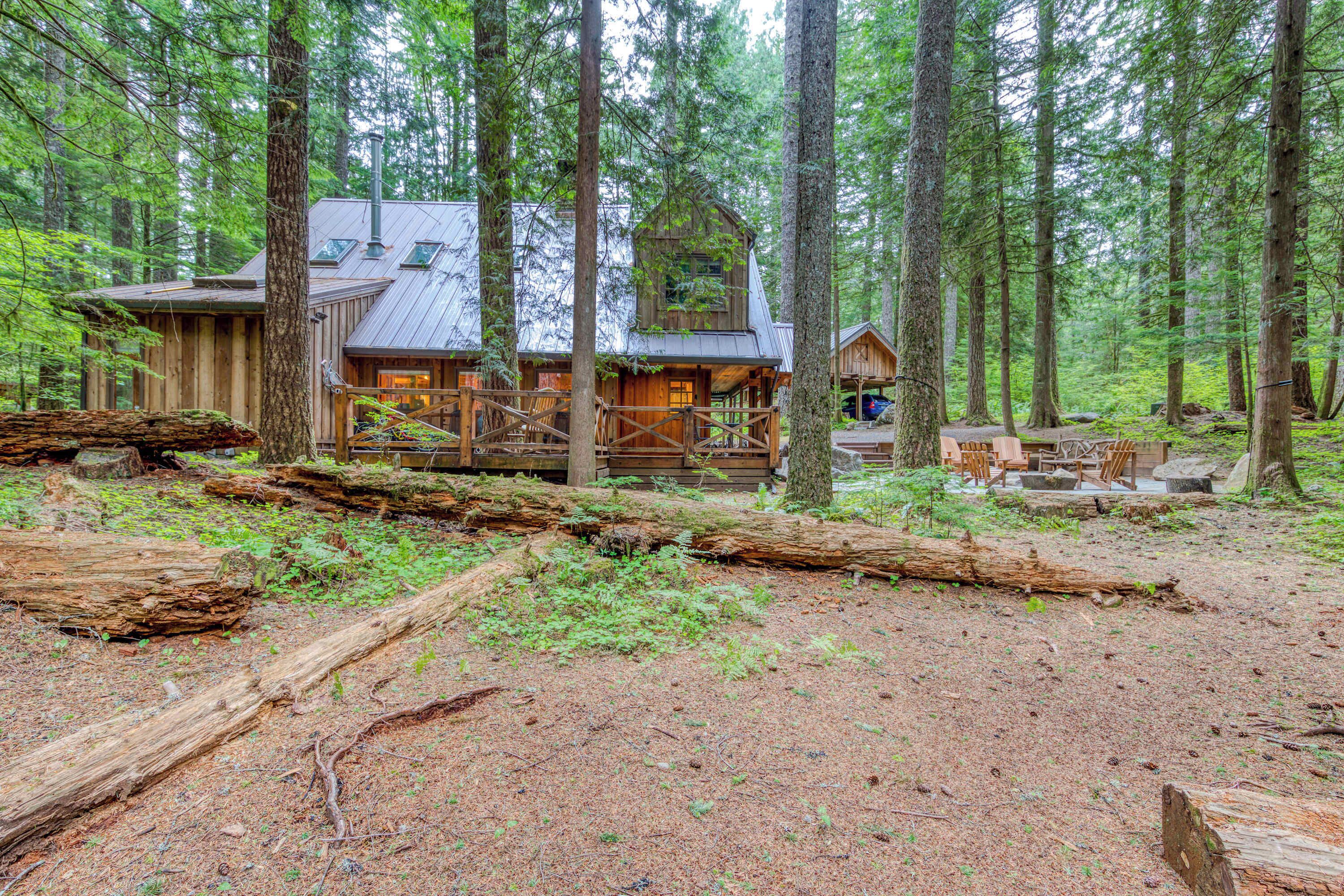 A rustic cabin with a deck, surrounded by tall trees in a forest.