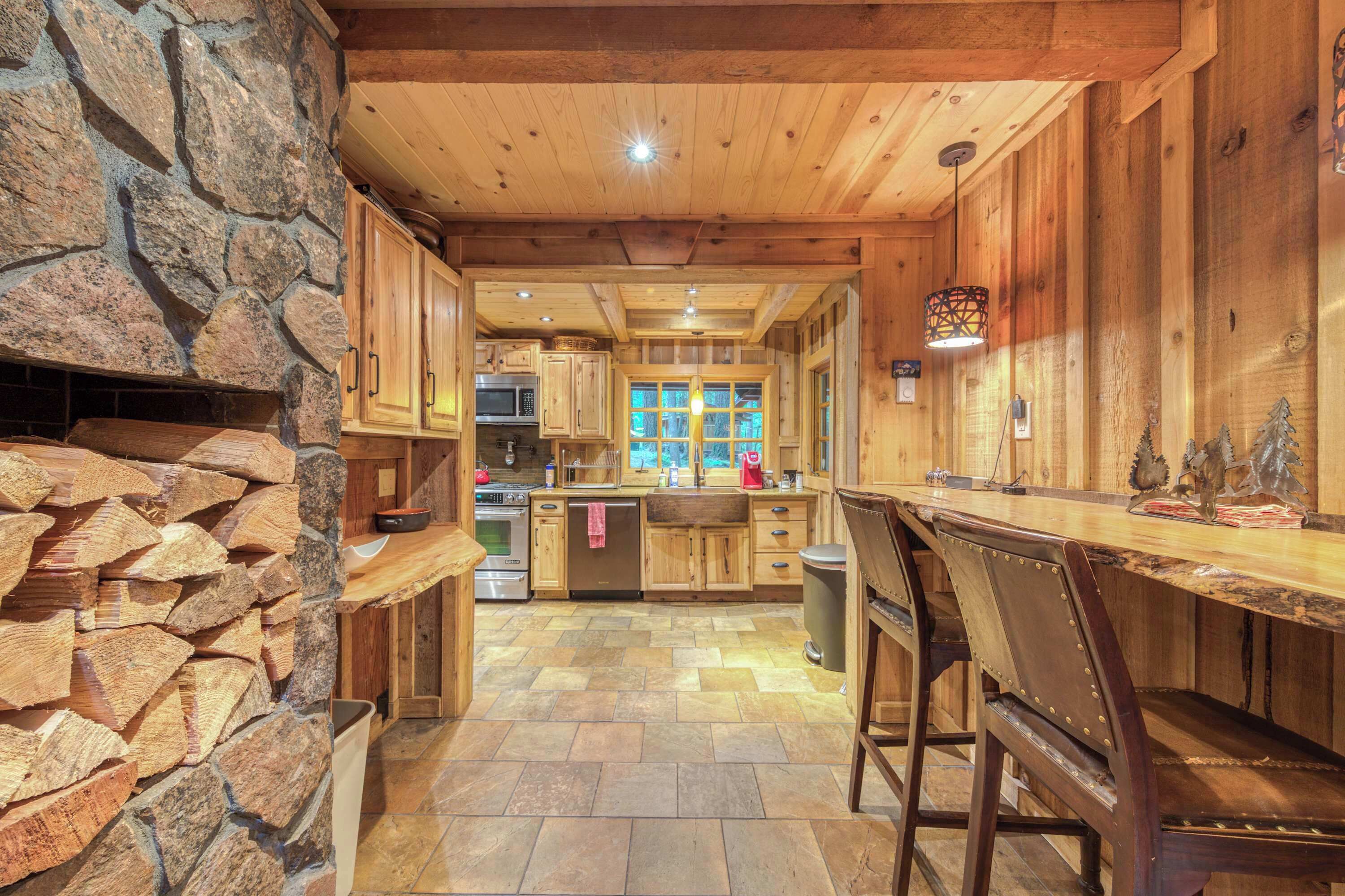 A rustic kitchen with stone walls, wooden cabinets, and a bar area with stools.