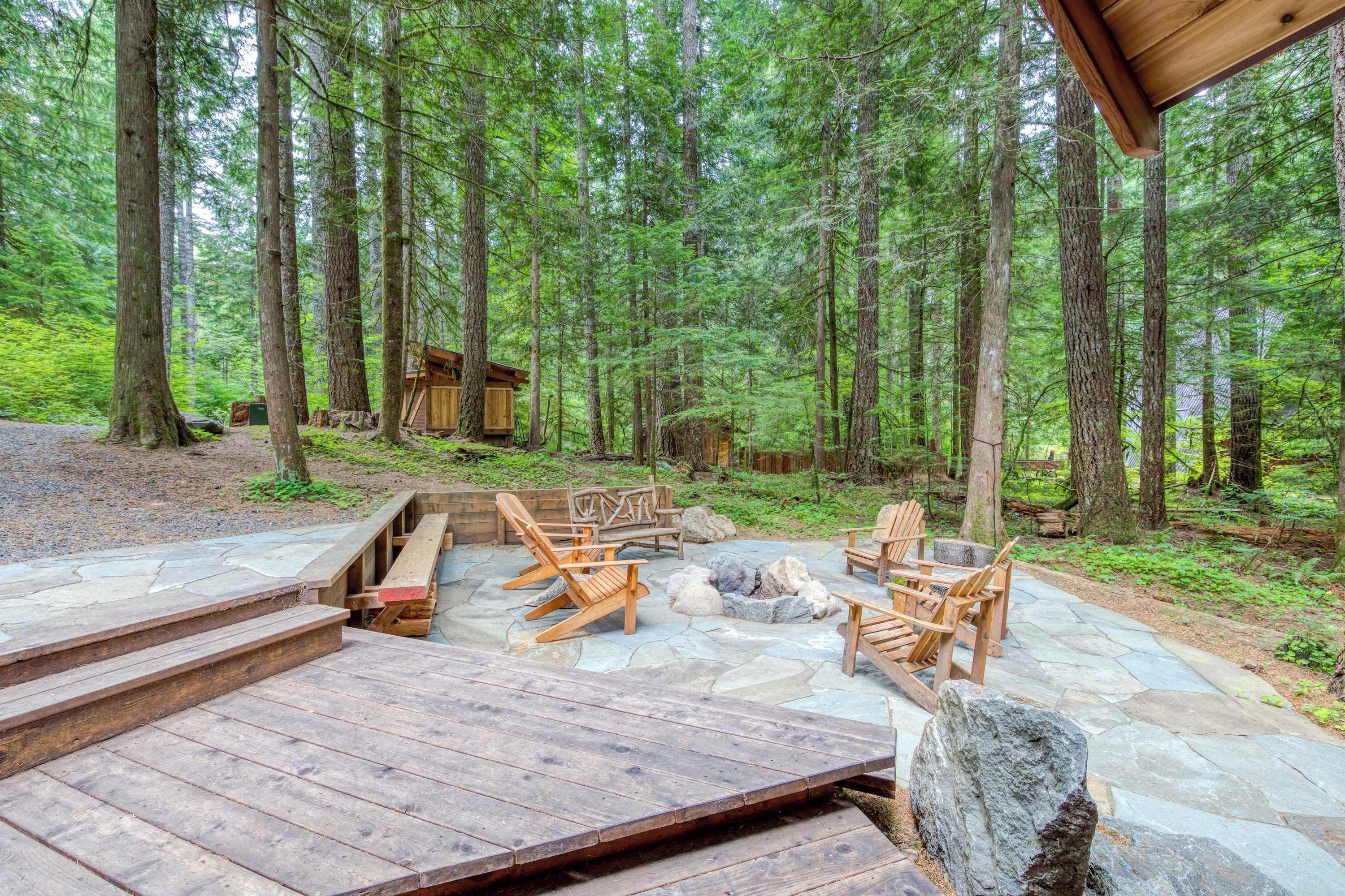 A wooden deck with outdoor seating and a fire pit, surrounded by a forested area.