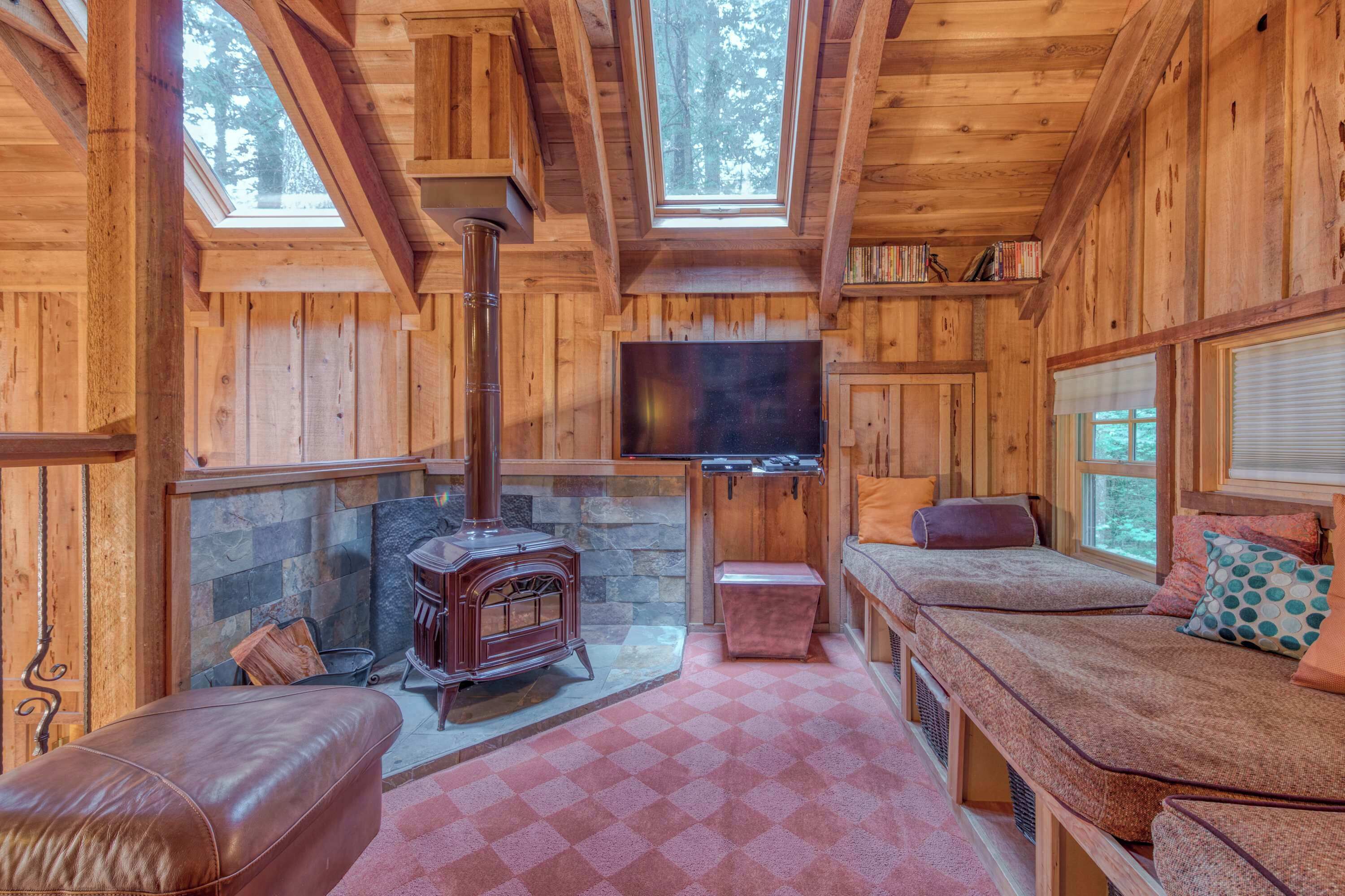 A log cabin interior with a stone fireplace, wooden walls, a television mounted on the wall, and a bench with cushions.