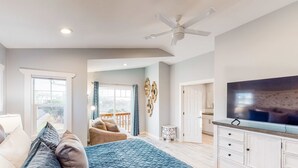 Un dormitorio con cama, televisión, ventilador de techo y vistas al exterior.