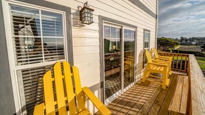 Una terraza de madera con sillas Adirondack amarillas, una puerta de cristal y una pared exterior blanca.
