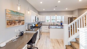 Una cocina moderna con armarios blancos, una isla central, iluminación colgante y una escalera que sube a otro nivel.