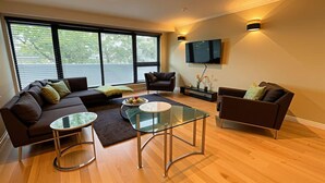 Una sala de estar moderna con un sofá, sillones, una mesa de centro de vidrio y un televisor de pantalla plana montado en la pared.