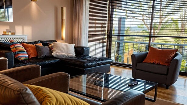 Una sala de estar moderna con un sofá de cuero negro, una mesa de centro de vidrio y un sillón gris.