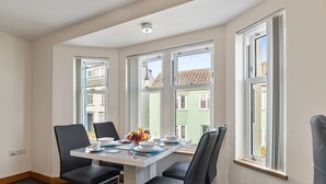 A dining area with a table set for four, large windows, and a view of buildings outside. - Sea Steam Apartment - Close to Village and Beach (Saundersfoot)