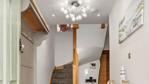 A narrow hallway with a bench, a staircase, a small table with a towel, and a wall-mounted clock. - Sea Steam Apartment - Close to Village and Beach (Saundersfoot)