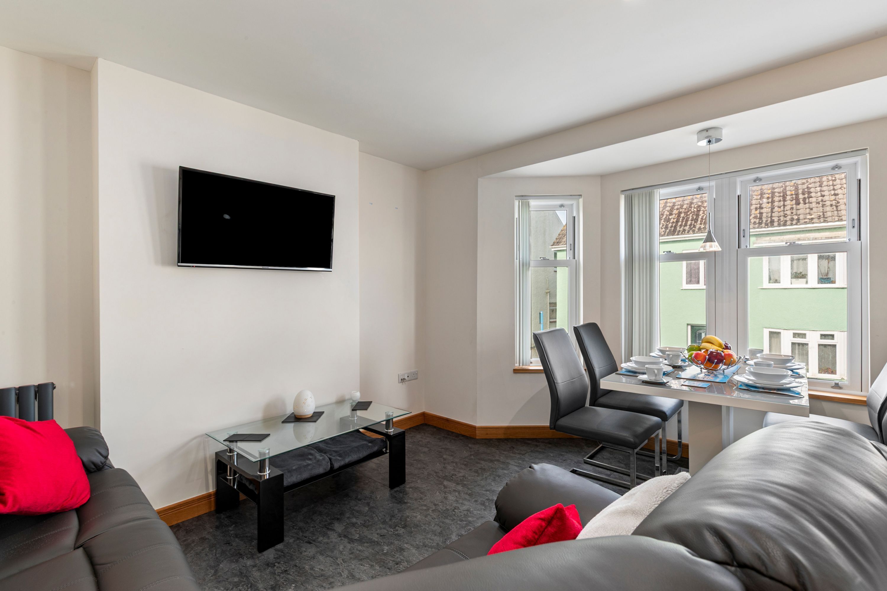 Ett modernt vardagsrum med en platt-TV, ett soffbord i glas, en soffa och en matplats med stolar och ett bord som är dukat för en måltid.