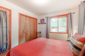 A bedroom with a bed, a wooden wardrobe, a window with curtains, and a small table.