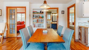 A dining area with a wooden table, blue upholstered chairs, a hanging pendant light, and a bookshelf in the background.