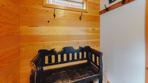 A wooden bench with a window above it, a wall-mounted picture, and a wooden beam with hooks.