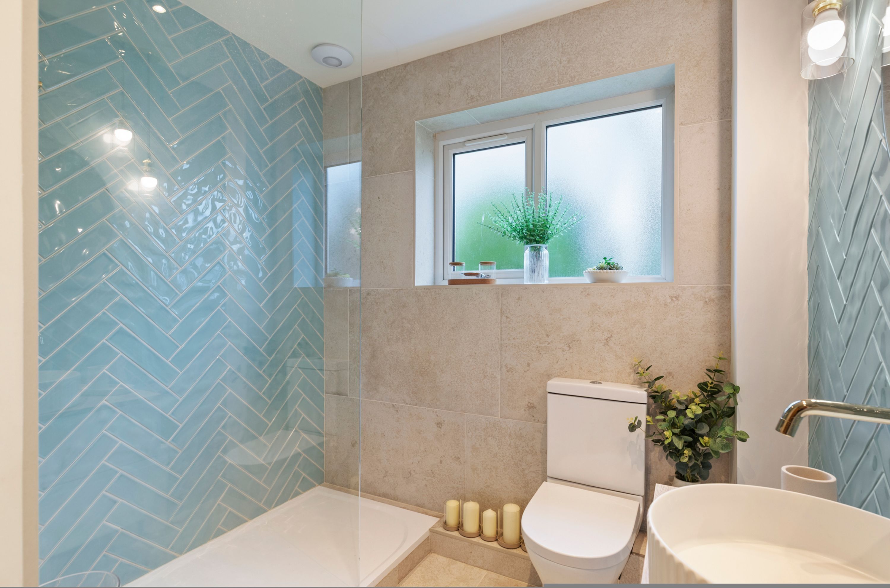 Une salle de bain avec une baignoire, des toilettes et un lavabo, une fenêtre avec une plante, et un motif de carrelage en chevrons sur les murs.