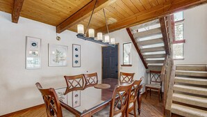 Uma sala de jantar com uma mesa de vidro, cadeiras de madeira, um candelabro e uma escada.