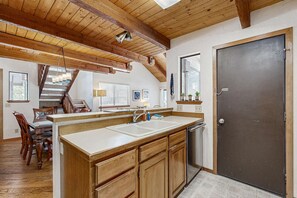 A kitchen with wooden cabinets, a large island, a dark door, and a staircase leading to another level. - Inviting condo with private sauna & wonderful shared amenities (Sunriver)
