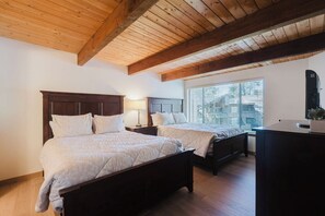 A bedroom with two beds, wooden beams on the ceiling, a window with blinds, and a desk with a computer. - Inviting condo with private sauna & wonderful shared amenities (Sunriver)