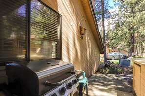 Eine Holzaußenwand, ein Fenster mit Jalousien, ein Grill und ein Stuhl.