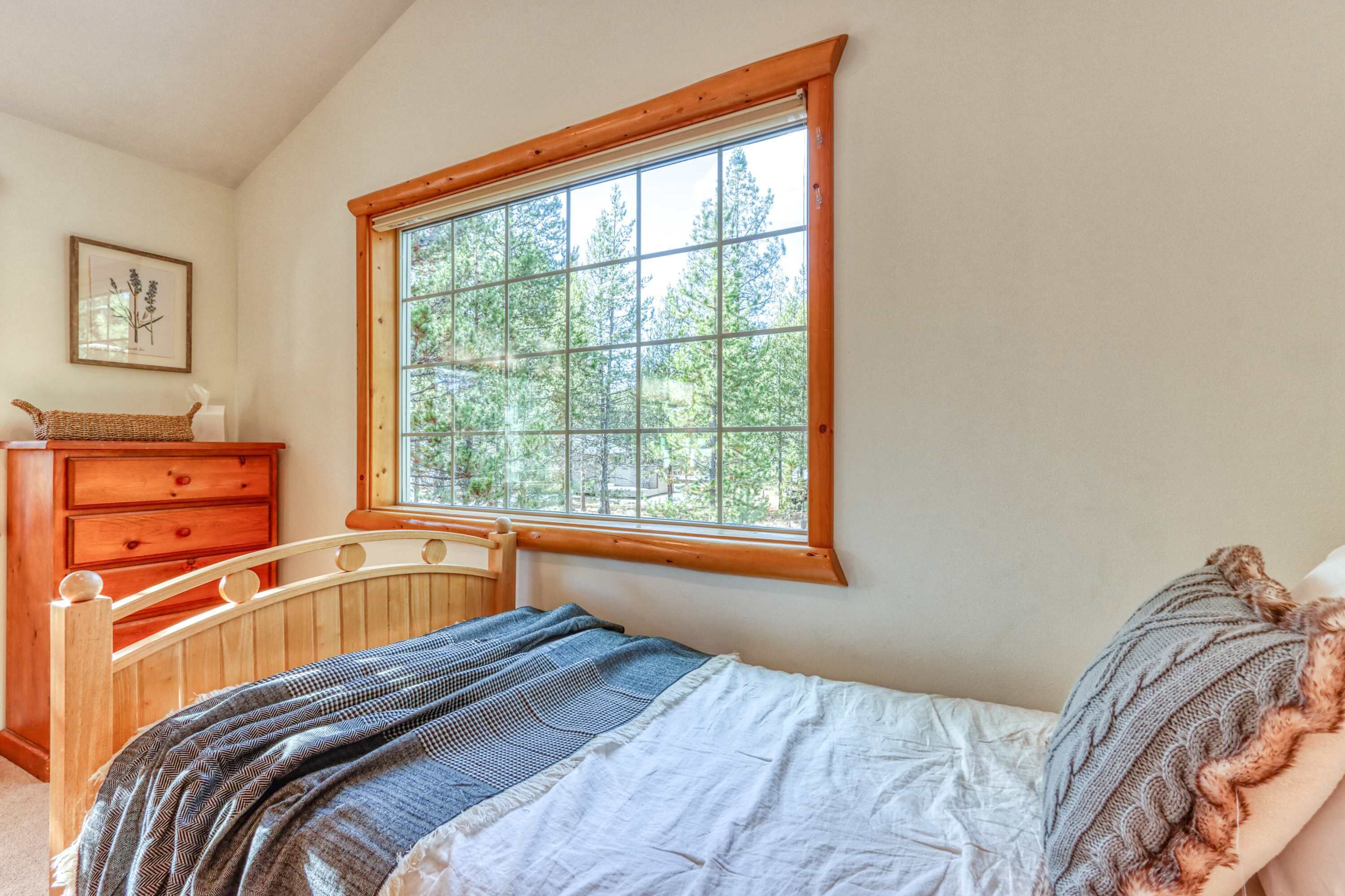 Una camera da letto con un letto in legno, una finestra vista alberi, un comò e un quadro appeso al muro.