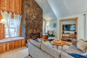 A cozy living room with a stone fireplace, a large TV, and comfortable seating. - Spacious home with free WiFi, private hot tub, shared pool, & SHARC passes (Sunriver)