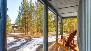 Ein überdachter Balkon mit einem Holzstuhl, Blick auf einen Wald und schneebedeckten Boden.