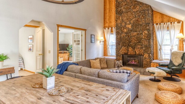 Ein gemütliches Wohnzimmer mit Kamin aus Stein, Holzboden und einem Essbereich mit Holztisch.