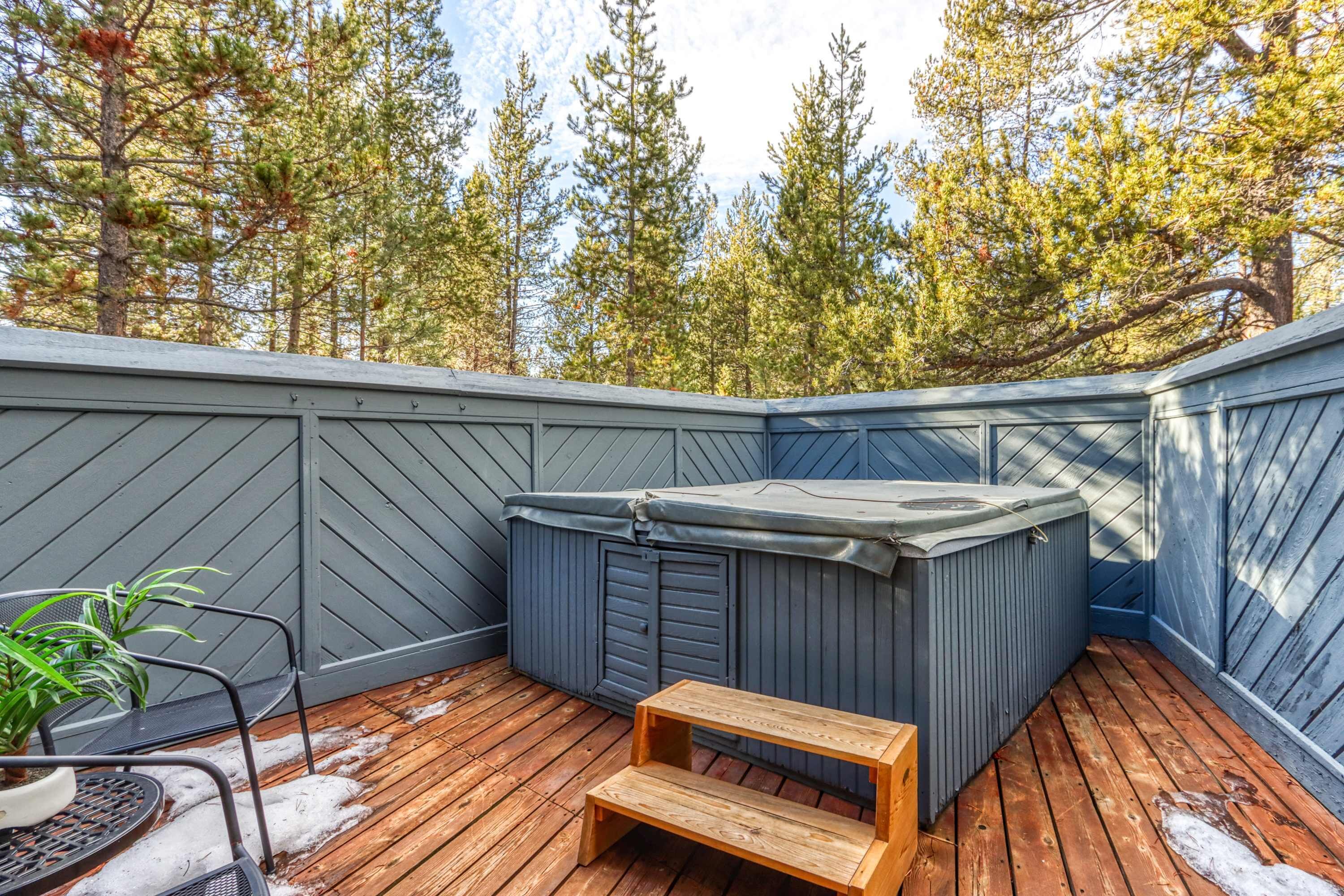 A wooden deck with a hot tub, a wooden bench, and a chair.