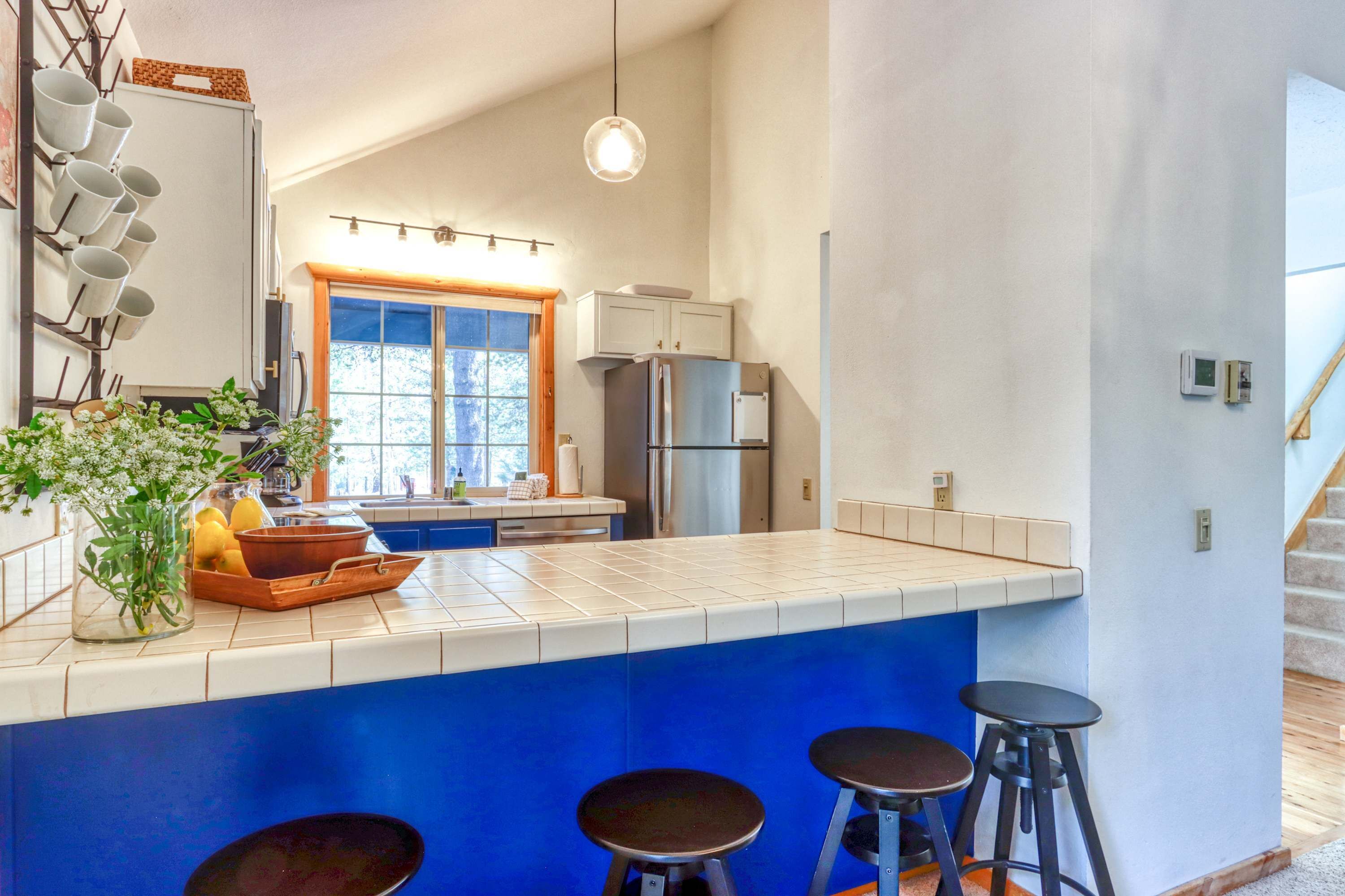 Eine Küche mit blauer Akzentwand, einer zentralen Kochinsel mit Sitzgelegenheiten, einem Kühlschrank und einem Fenster mit Aussicht.