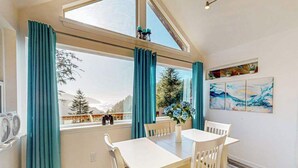 A dining area with a table and chairs, a window with curtains, and a view of trees and mountains.